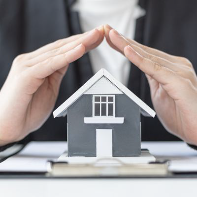 Small model house with hands held over it representing insurance coverage