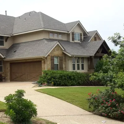 tan house with gray-brown shingles, brown garage door, and driveway in the foreground 